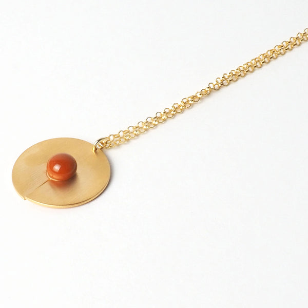 Orange open disc pendant from the PIB collection by PLATÓNICA. Gold plated silver and glass. Minimalist jewelry. Contemporary jewelry. Author jewelry. Made in Granada, Andalusia, Spain. Jewelry workshop in the Albaicín. Crafts. Hand-made jewelry. Jewels made from Andalusia. Geometry. Modern and sophisticated style.